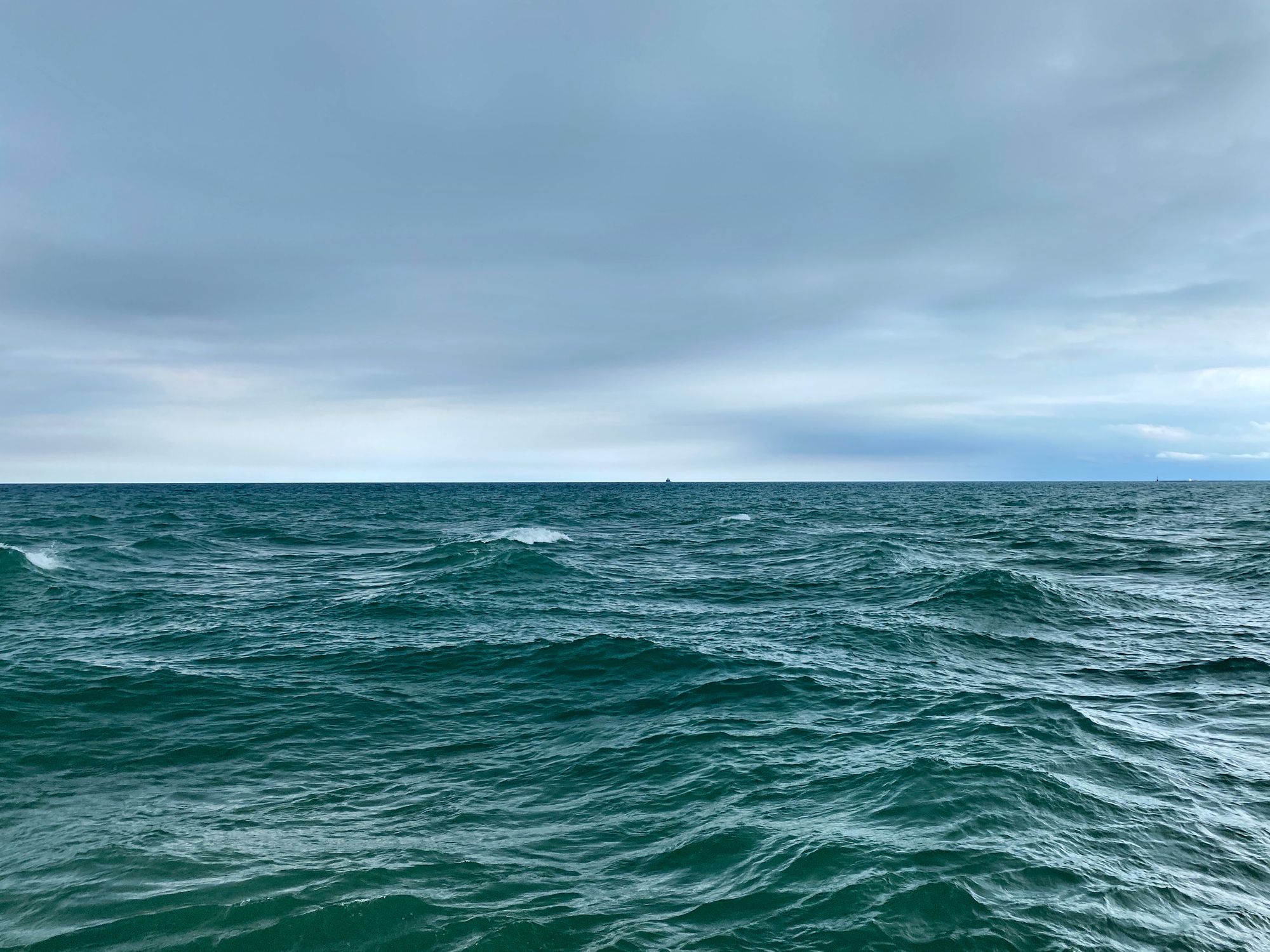 Pale blue clouded sky above a choppy, dark green-blue lake surface