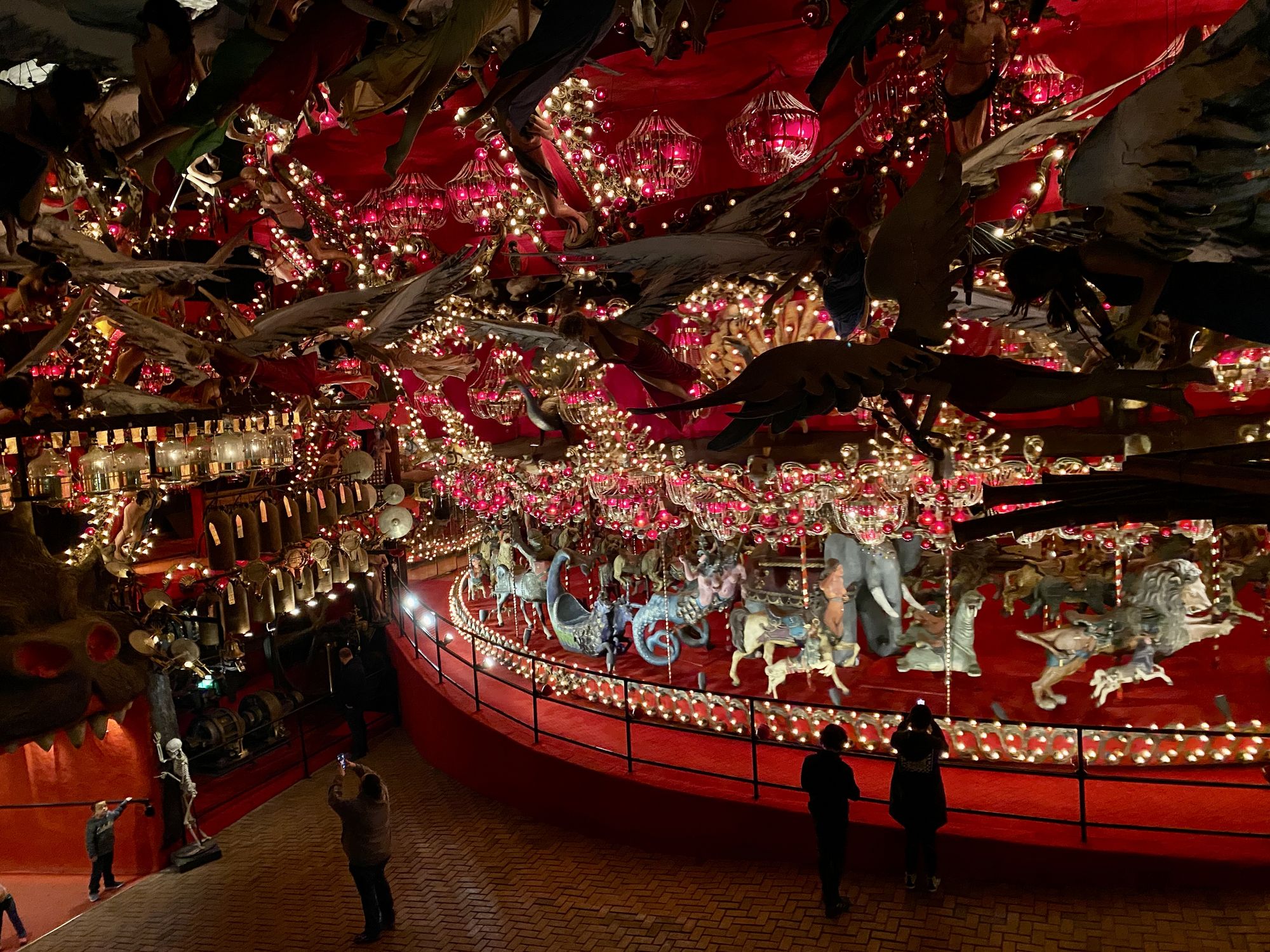 A gigantic, brightly-lit carousel, rimmed in red, with mannequins-as-angels sweeping the ceiling above it