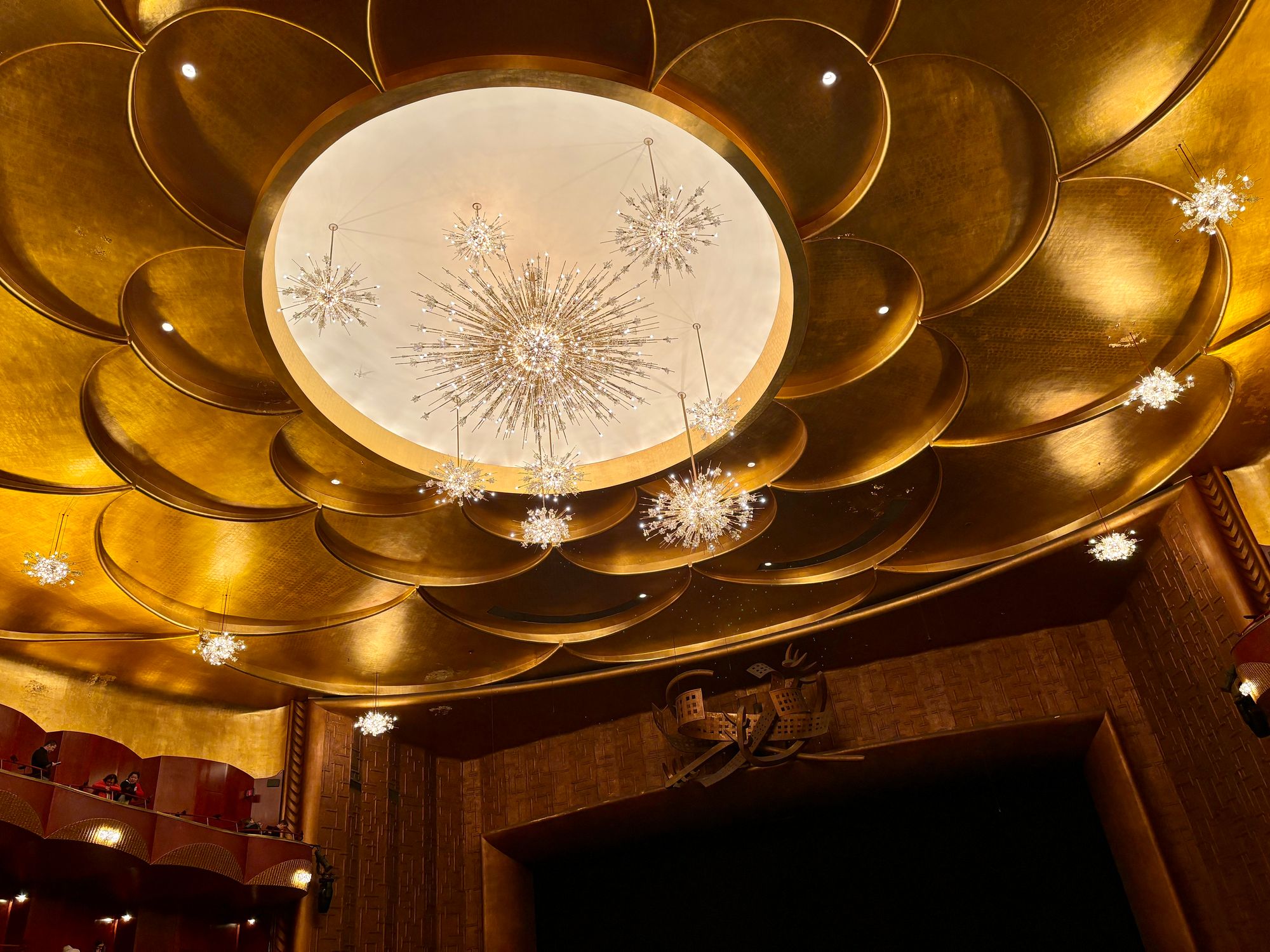 Ceiling of the Metropolitan Opera, set with layered gold circular panels and a bright center from which starburst chandeliers hang