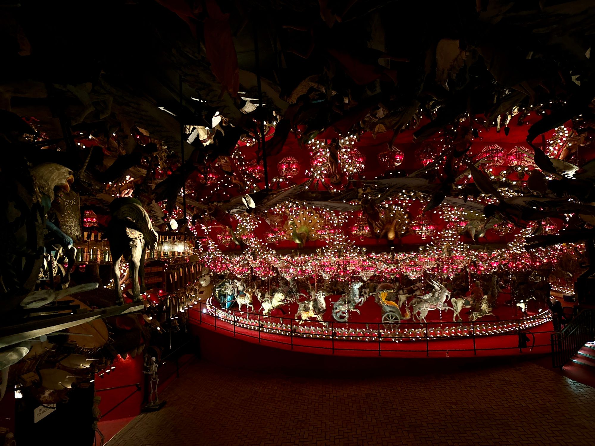 A massive, elaborate red carousel studded with hundreds of lights inside a large, dark room