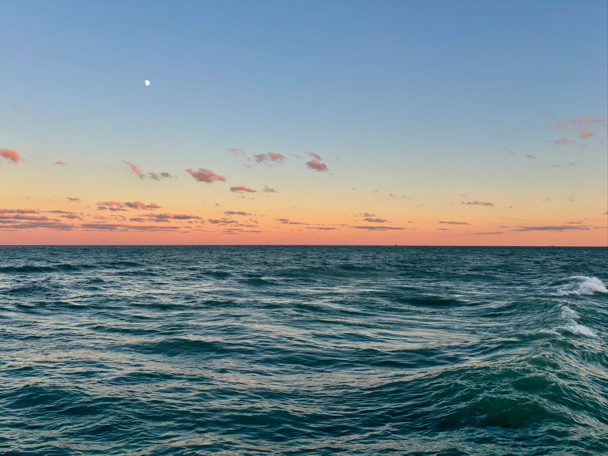 Lake horizon at sunset with a small pale moon overhead