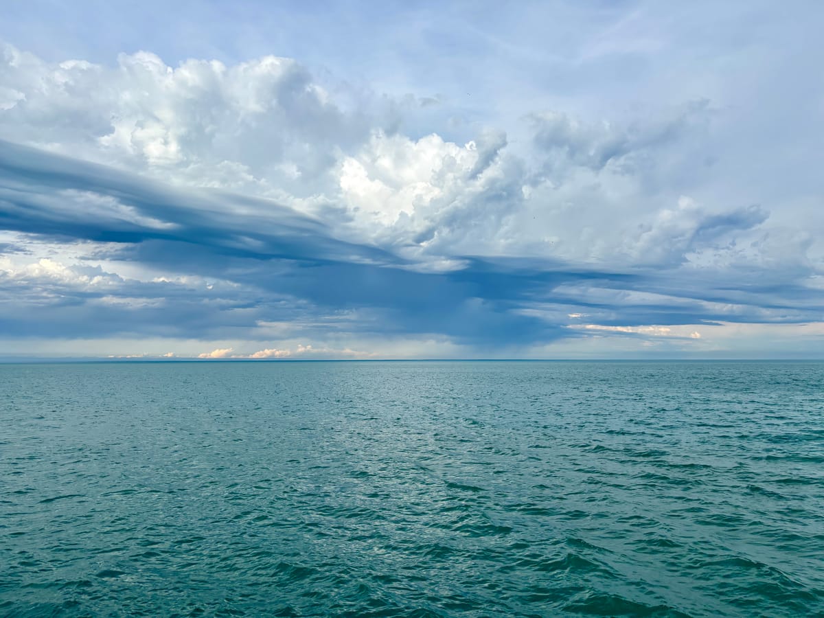 The horizon of Lake Michigan with a cloud-swept sky above and calm blue-green water below.