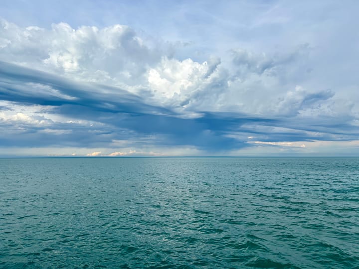 The horizon of Lake Michigan with a cloud-swept sky above and calm blue-green water below.